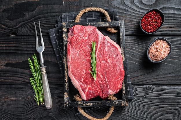 Runder rauwe filet voor steaks in een houten dienblad met kruiden. Zwarte houten achtergrond. Bovenaanzicht.