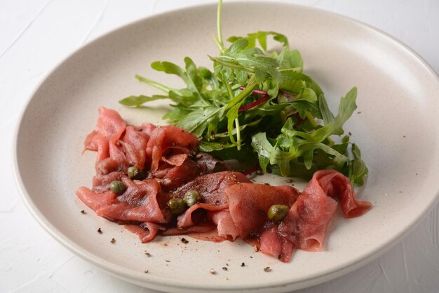 Rundercarpaccio met Parmezaanse kaas, kappertjes en rucola. Met olijfolie en sojasaus