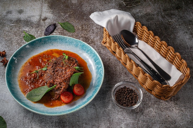 Runderstoofpot met bouillon en kruiden in een blauw bord met kruiden en zwarte peper tegen een grijze stenen tafel