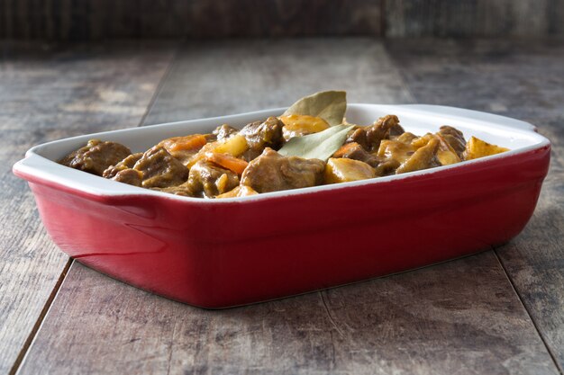 Rundvlees gestoofd met aardappelen, wortelen en specerijen in keramische pot op houten tafel