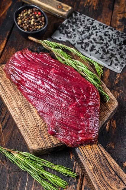 Rundvlees rauw vlees steak op een cuuting bord met rozemarijn. Zwarte tafel. Bovenaanzicht.