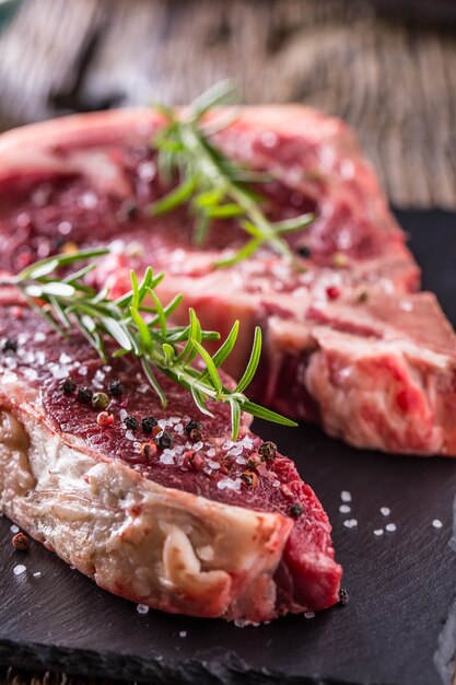 Rundvlees rauwe biefstuk. Rauwe verse T-bone steak met zoute peper en rozemarijn.