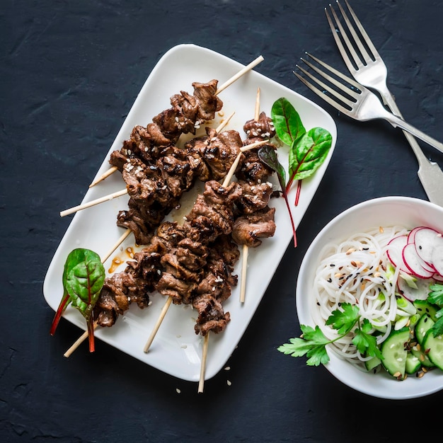 Rundvlees spiesjes en rijst noedels groenten salade op een donkere achtergrond bovenaanzicht Aziatische stijl eten