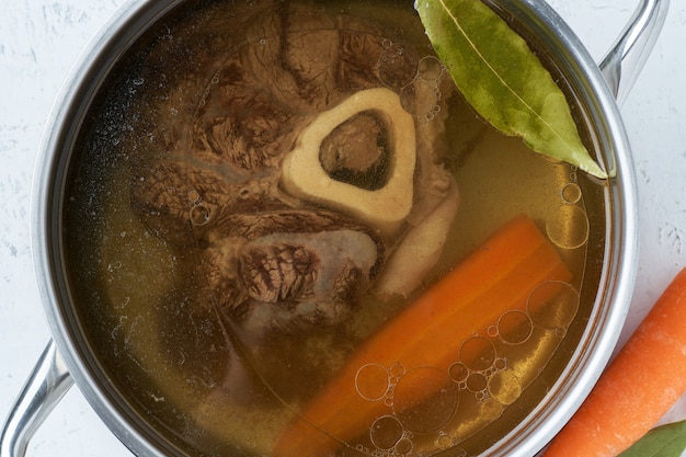 Rundvleesbouillon, ossobuco op been, rijke soep in steelpan, lang langzaam wegkwijnen.