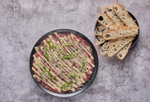 Rundvleescarpaccio koud voorgerecht met Parmezaanse kappertjes en rucola op zwarte plaat