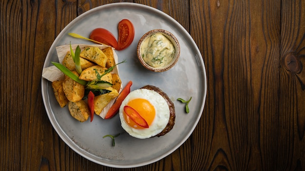 Rundvleesmedaillons met ei, aardappelen en paprika op een houten tafel