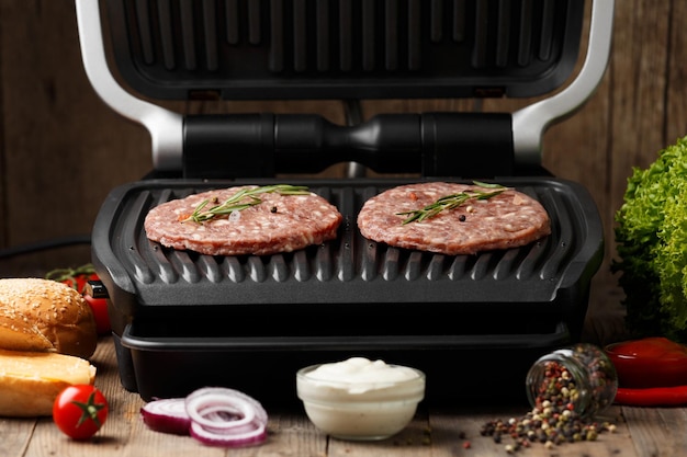 Rundvleespasteitjes voor een burger worden gebakken op een slimme elektrische grill op een rustieke houten achtergrond Zelfgemaakte hamburgers koken Ingrediënten voor hamburgers