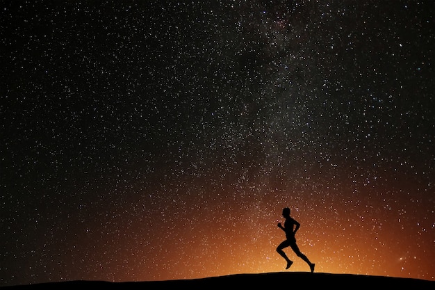 Atleta corridore in esecuzione sulla collina con sfondo bellissimo notte stellata. siluetta dell'allenamento da jogging dell'uomo in tempi bui, concetto di benessere.