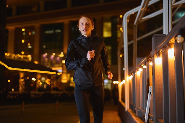 Runner atleet fitness en sport motivatie sterke atletische vrouw die in nacht stad loopt met gele ...