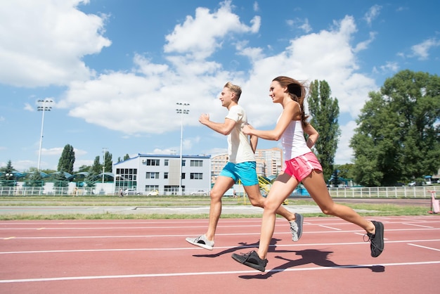 Runner on competition and future success. Coach and trainer at workout. Sport and healthy fitness. Man and woman sunny outdoor on blue sky. Couple running on arena track.