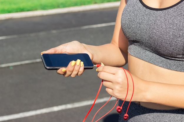 Runner girl holding smartphone and inserts headphones on the phone. Training in the morning time. People sport and fitness concept