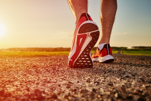 Runner man feet on road at the sunset