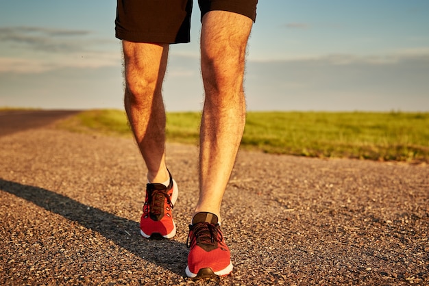 Runner man feet on road at the sunset