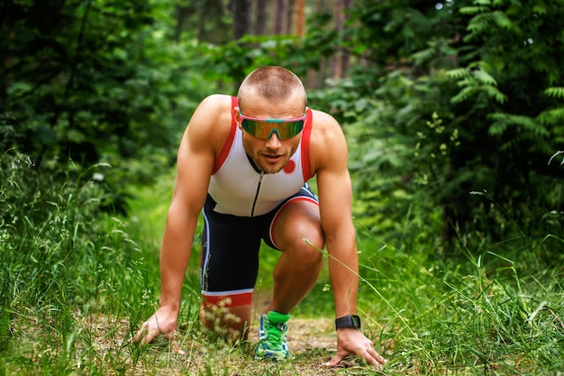 Runner man in sunglasses ready for quick start in the forest.