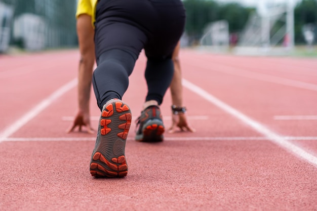 Runner standing in low start position ready to run along red rubberized track on ground