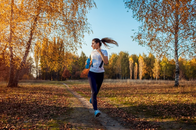 Runner training in autumn park, Woman running with water bottle at sunset, Active lifestyle