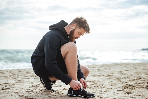 Corridore che allaccia i lacci delle scarpe sulla vista laterale della spiaggia