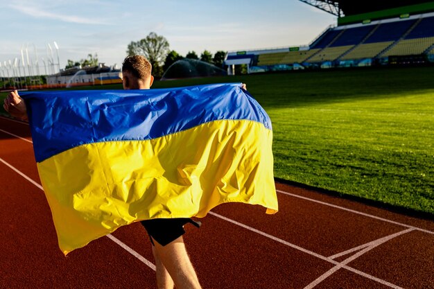 Foto un corridore con una bandiera blu e gialla sulle spalle corre su una pista.