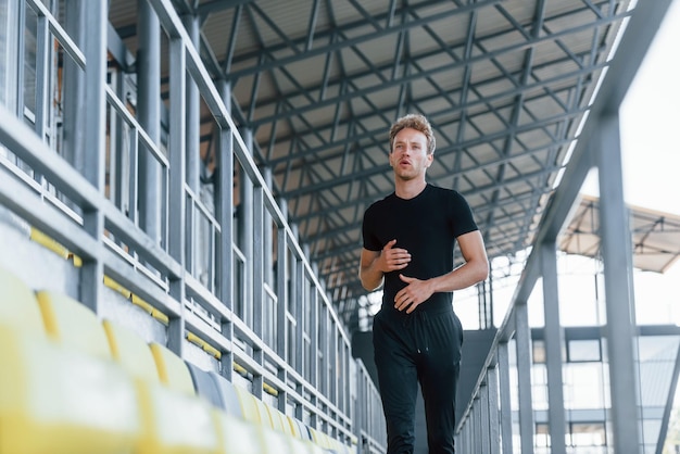 Running on the bleachers Sportive young guy in black shirt and pants outdoors at daytime