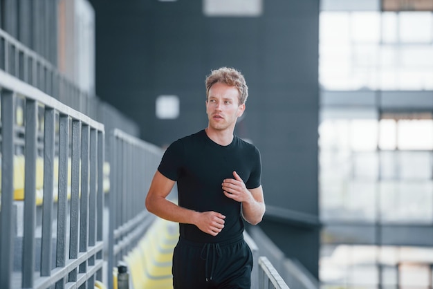 Running on the bleachers Sportive young guy in black shirt and pants outdoors at daytime