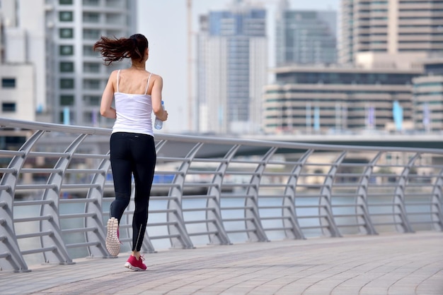 Running in city park. Woman runner outside jogging at morning with Dubai urban scene in background