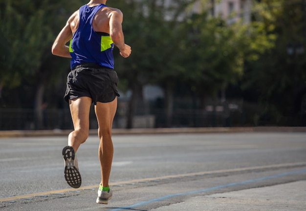 Running in the city roads Young man runner back view blur background