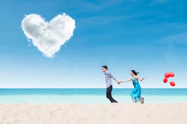 Foto coppia in corsa sulla spiaggia sotto una nube di cuore