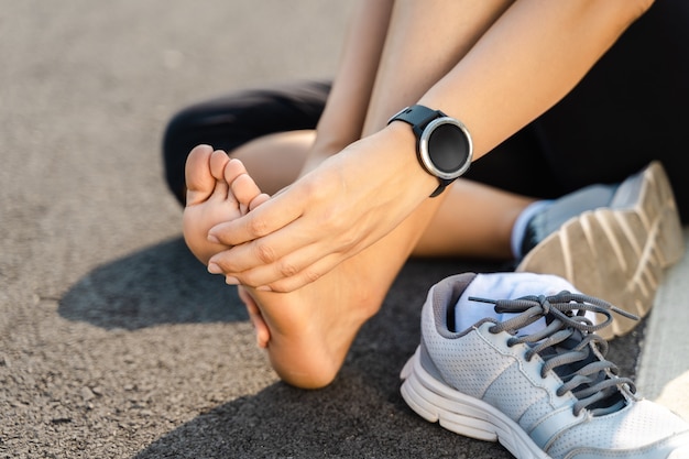 Running injury leg accident- sport woman runner hurting holding painful sprained ankle in pain. Female athlete with joint or muscle soreness and problem feeling ache in her lower body.