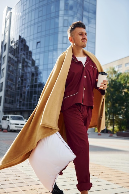 Running late for the work Young man in pajama is outdoors on the street Feels sleepy