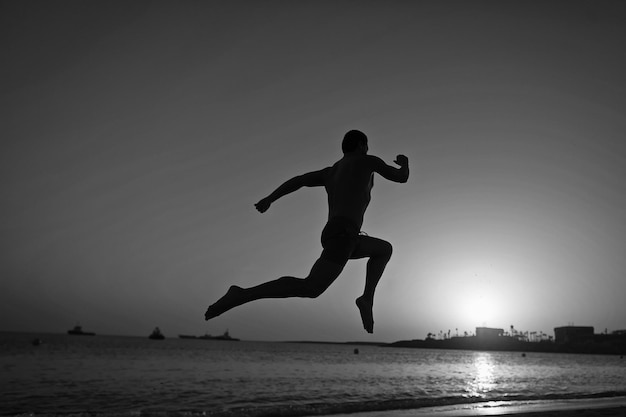 Running man silhouette of running man on sunset fiery sky background in sea sport and recreation future and success people and nature speed and healthy lifestyle