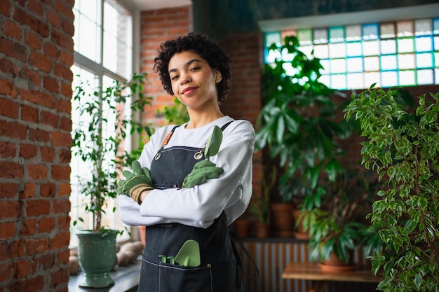 写真 自社事業を営むアフリカ人女性花屋が緑色の植物の植物店でエプロンを着用している