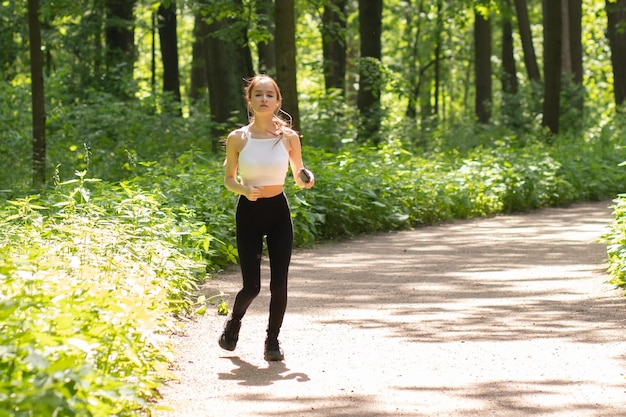 Correre facendo sport tenendosi in forma la ragazza corre in cuffia nel parco tra gli alberi