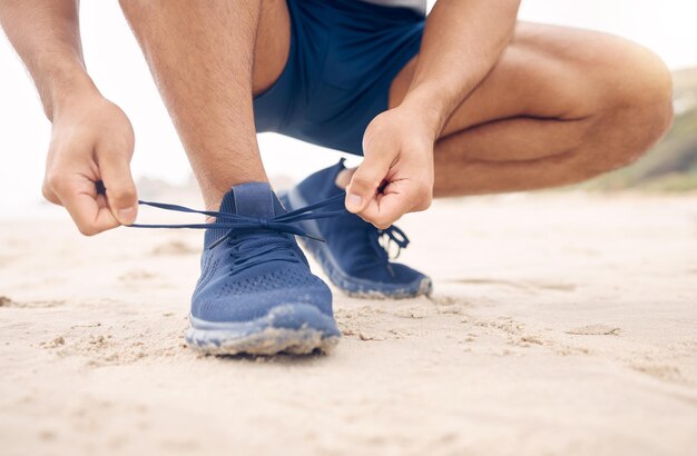 Running shoes hands and fitness man at a beach for training exercise or morning cardio zoom Legs closeup and male runner with sneakers lace outdoor for wellness workout or marathon practice run