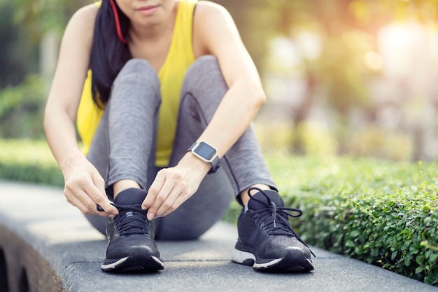 ランニングシューズ - 靴ひもを結ぶ女、庭でジョギングの準備をしているスポーティなフィットネスランナー。