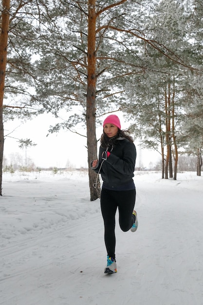 Running sport vrouw Vrouw joggen in het winterbos met sportieve hardloopkleding en telefoons