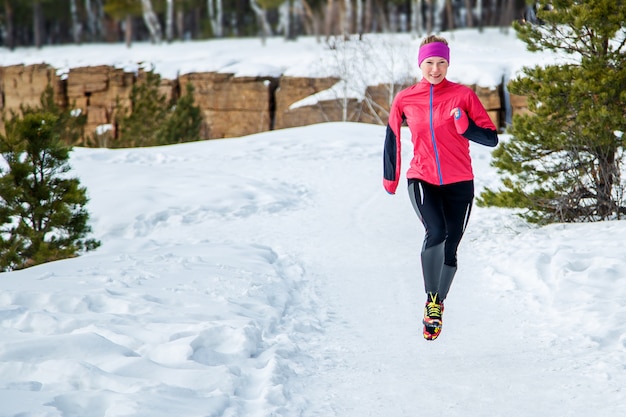 スポーツ女性を実行しています。暖かいスポーティなランニング服を着て寒い冬の森でジョギングする女性ランナー。