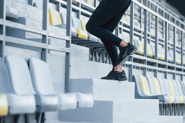 Foto correre sulle scale giovane sportivo in camicia nera e pantaloni all'aperto durante il giorno