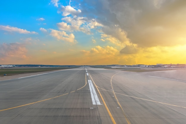 Pista dell'aeroporto nei cumuli di colore giallo di pendenza di azzurro del cielo della luce del sole di tramonto.