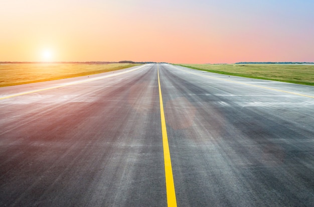 Асфальт взлетно-посадочной полосы в аэропорту утром на рассвете закат солнечный свет