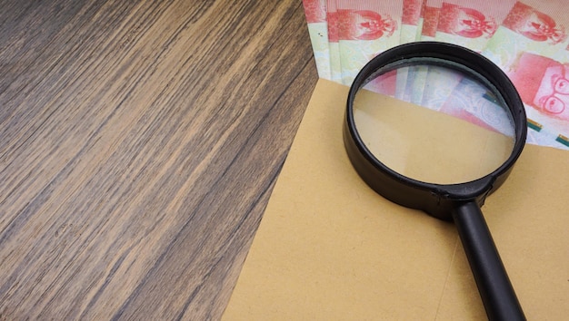 Rupiah money in envelope with magnifying glass are lying on wooden table