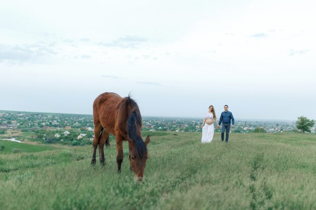 Rural couple on a green meadow communicates with animals. Pregnant wife. Therapy and relaxation for pregnant women.