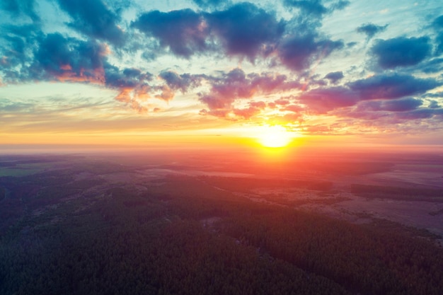 Rural landscape in the morning with a beautiful burning sky Bird'seye Panoramic view of pine forest fields river and village during bright sunrise