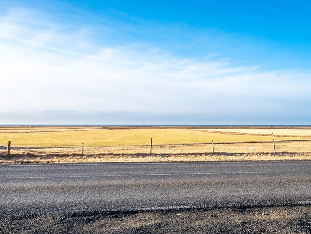 Rural road on drive trip under cloudy blue sky in Iceland