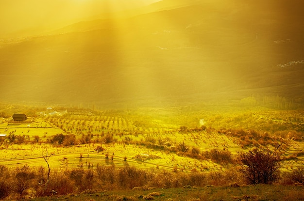 緑の丘、劇的な空の山々と太陽光線のある田舎の夕日の風景