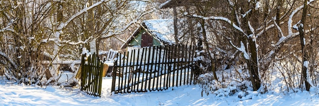 雪に覆われた木々、柵、庭の古い家のある田園風景