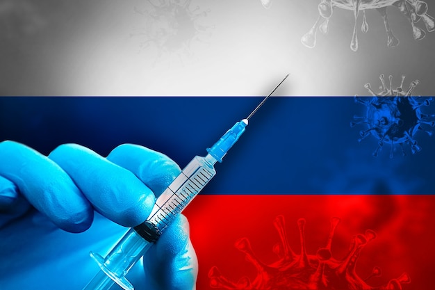 Russia Covid19 Vaccination Campaign Hand in a blue rubber glove holds syringe in front of flag