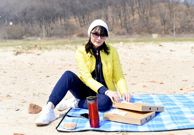 Русская 45-летняя женщина собирается есть пиццу сидя на пляже