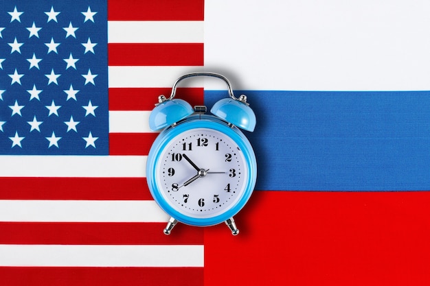 Russian and American flags and the clock as a symbol of political relations. Creative top view flat lay of Russia and USA flag alarm clock. Concept of confrontation between USA and Russia