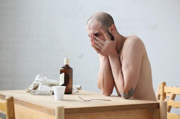 Russian drunk sitting at the table and sad. He closes her face