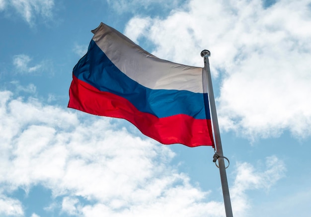 Russian flag or flag of Russian Federation waving on flagpole against blue sky